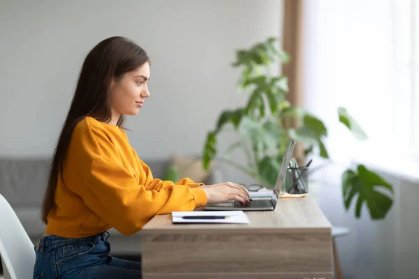 Jovem mulher caucasiana feliz comunicando on-line via laptop pc, sentado na mesa dentro de casa, espaço de cópia — Fotografia de Stock