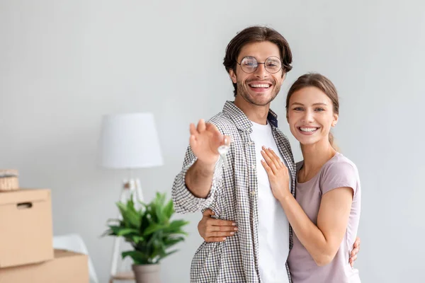 Satisfecho joven caucásico esposa y marido en gafas muestran las llaves en su propio piso en la habitación con cajas de cartón embaladas —  Fotos de Stock