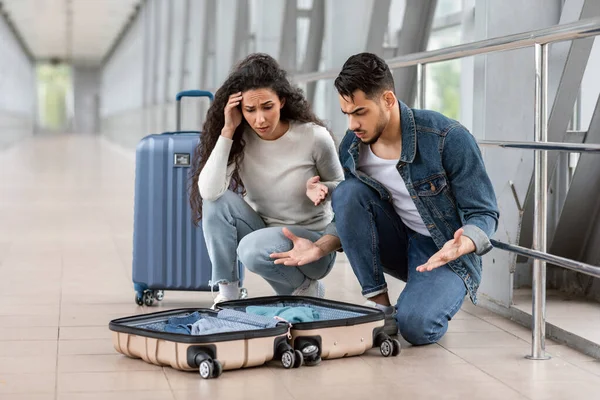 Objetos perdidos. Confundida pareja árabe joven sentado cerca de la maleta abierta en el aeropuerto — Foto de Stock