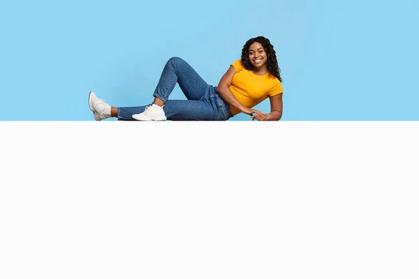 Šťastná černoška ležící na obrovské prázdné plakátu přes modrou — Stock fotografie