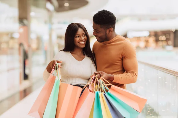 Feliz pareja negra sosteniendo bolsas de compras mirándose —  Fotos de Stock