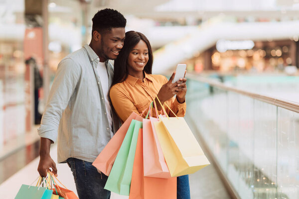 Портрет возбуждённых чёрных супругов, использующих телефон в торговом центре