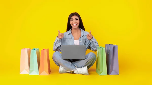 Happy vrouw met boodschappentassen met behulp van laptop tonen als — Stockfoto