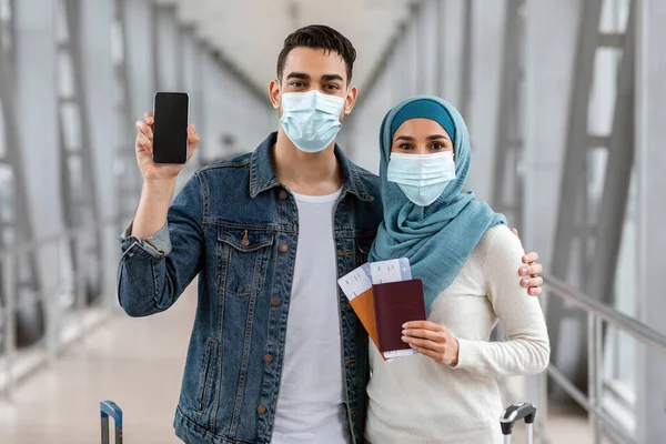 Los cónyuges islámicos que usan máscaras faciales médicas en el aeropuerto que demuestran el teléfono inteligente en blanco —  Fotos de Stock