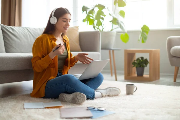 Νεαρή γυναίκα που κάθεται στο πάτωμα με φορητό υπολογιστή και ακουστικά, σπουδές στο διαδίκτυο, έχοντας απομακρυσμένη δουλειά, τηλεδιάσκεψη στο σπίτι — Φωτογραφία Αρχείου