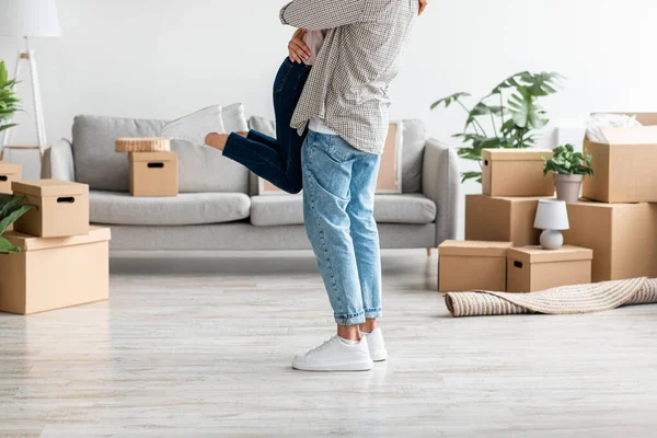 Feliz milenar marido caucasiano em aumentos casuais e abraços esposa no quarto com caixas de papelão com pertences — Fotografia de Stock