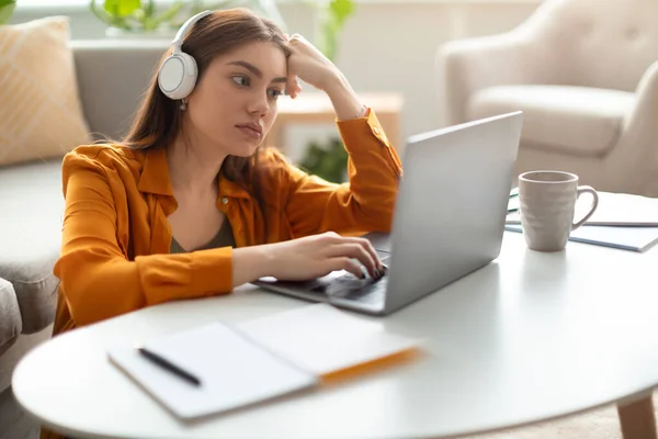 Serieuze jonge vrouw met een laptop die een koptelefoon draagt, online werkt of studeert, videochats heeft op kantoor — Stockfoto