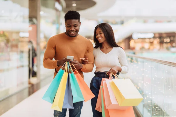 Retrato de una feliz pareja negra usando bolsas de compras con soporte telefónico — Foto de Stock