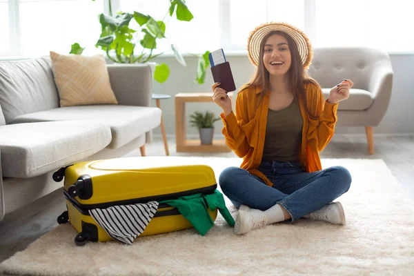 Nadšená mladá žena drží pas a jízdenku v blízkosti jasně zabalený kufr doma — Stock fotografie