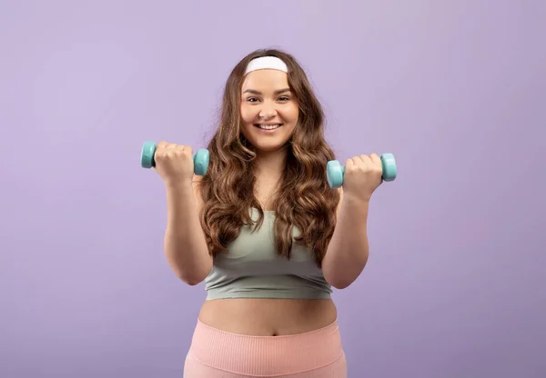 Blij glimlachen opgewonden plus size Europese millennial dame in sportkleding tillen halters, op violette achtergrond, studio — Stockfoto