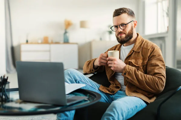 Людина дивиться фільм онлайн на ноутбуці п'є каву вдома — стокове фото
