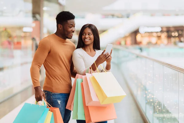 Retrato de cónyuges negros excitados usando bolsas de compras con soporte telefónico —  Fotos de Stock