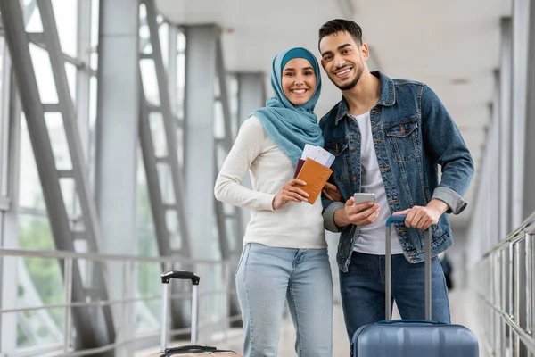 Ritratto di felice coppia islamica in piedi all'aeroporto con bagagli e smartphone — Foto Stock