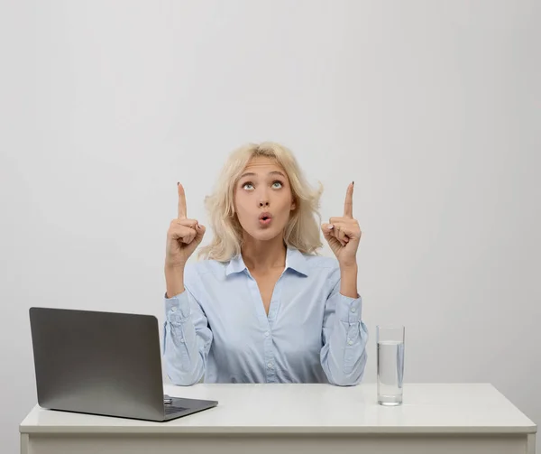 Masasında dizüstü bilgisayarıyla oturan, boş alana bakıp işaret eden sürpriz kadın ofis çalışanı. — Stok fotoğraf