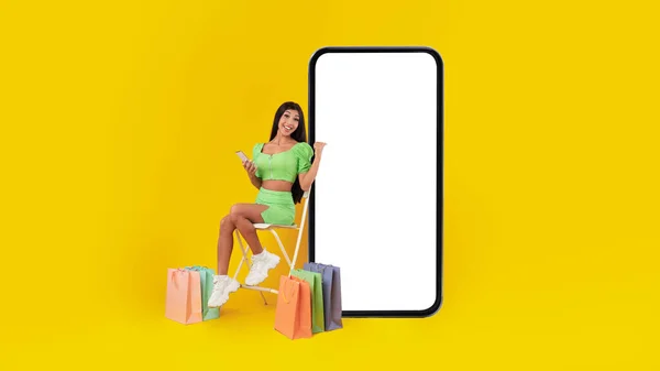 Frau sitzt neben weißem, leeren Smartphone-Bildschirm und Einkaufstaschen — Stockfoto