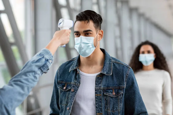 Viajes seguros. Cosas del aeropuerto Comprobación de la temperatura del pasajero árabe masculino en la máscara —  Fotos de Stock