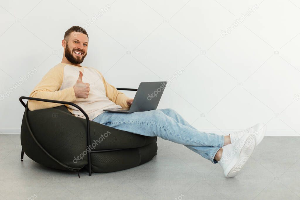 Man Using Laptop Gesturing Thumbs Up Sitting In Chair Indoor