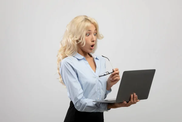 Geschokte zakenvrouw met laptop en kijken naar camera met open mond, verbaasd over carrière prestaties — Stockfoto