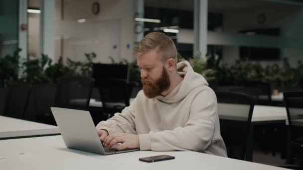 Barbudo chico usando ordenador portátil de trabajo sentado en la oficina moderna — Vídeo de stock