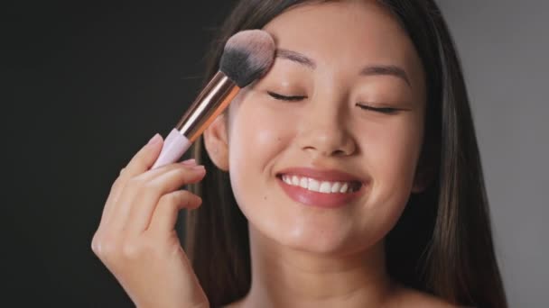 Idealny wygląd. Młoda piękna azjatycka kobieta co makijaż się, stosując różowy z profesjonalnym makijażu pędzel — Wideo stockowe