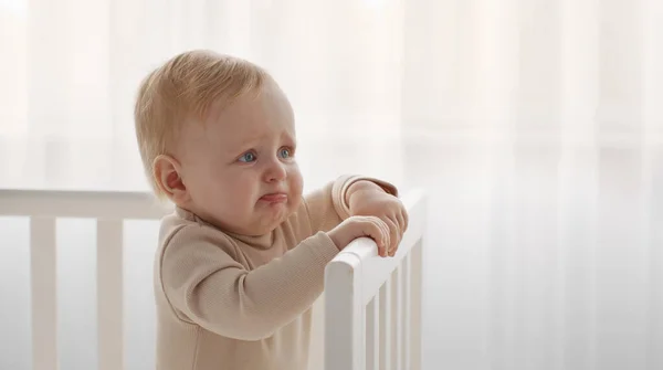 Gråter barnporträtt. Spädbarn trött och hungrig, börja gråta stående i spjälsängen, titta åt sidan på tomt utrymme — Stockfoto