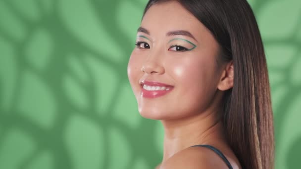 Young happy gorgeous woman with creative eye arrows smiling to camera, posing over green background with empty space — Stock Video