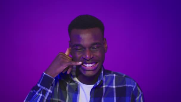 Чорний хлопець тримає руку близько вуха, як телефон, Пурпурне тло — стокове відео