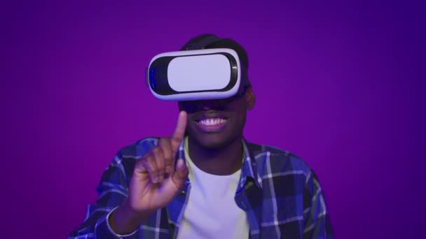 Hombre afroamericano experimentando realidad virtual usando auriculares, fondo púrpura — Vídeos de Stock