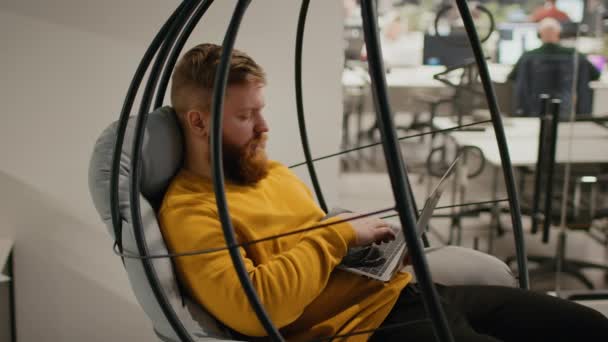Masculino usando laptop trabalho sentado no balanço cadeira no escritório — Vídeo de Stock