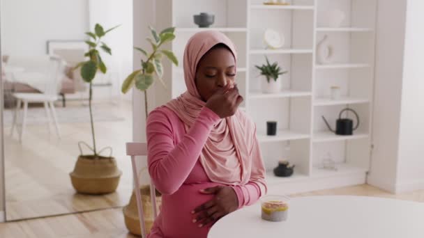 Szczęśliwy w ciąży czarny kobieta jedzenie chia budyń noszenie hidżab w pomieszczeniach — Wideo stockowe