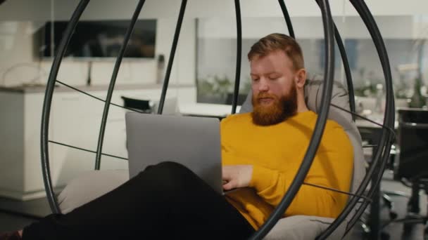 Homem usando laptop trabalhando sentado na cadeira de ovo no local de trabalho — Vídeo de Stock