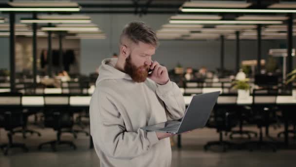 Homem barbudo falando no telefone usando laptop no espaço de co-trabalho — Vídeo de Stock