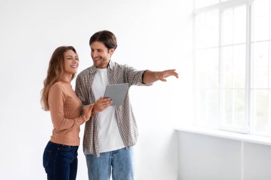 Yeni nesil Avrupalı kadın ve erkek, penceresi olan boş bir dairede tabletle yeni bir iç mekan planladıkları için mutlular.