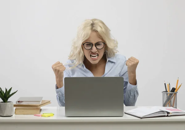 Розроблений працівник жіночого офісу сидить за столом з ноутбуком і сердиться на світлому фоні — стокове фото
