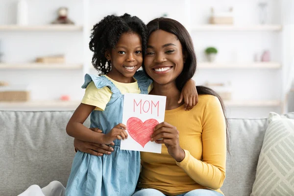 可爱的黑人女孩在家中向兴奋的妈妈赠送手工制作的贺卡 — 图库照片