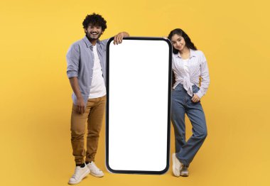 Heyecanlı genç Hintli erkek ve kadın dev akıllı telefonlara yaslanarak, uygulama veya web sitesini tanıtarak