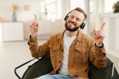 Kablosuz kulaklıkla müzik dinlemekten hoşlanan adam evde oturuyor.