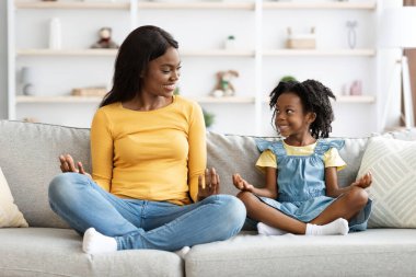 Aile hobileri. Mutlu siyah anne ve küçük kız evde birlikte meditasyon yapıyorlar.