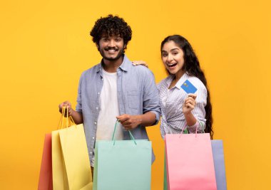 Tüketim konsepti. Kredi kartı ve alışveriş torbalarıyla heyecanlı Hintli çift uzaktan alışveriş yapıyorlar.