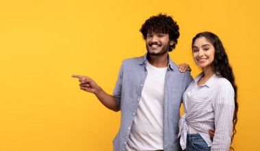 Şuna bir bak. Mesajın için yer gösteren mutlu Hintli çift, sarı arkaplanda boş alanı gösteren adam.