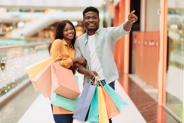 Šťastný černošky pár s nákupními taškami ukazuje na okno — Stock fotografie