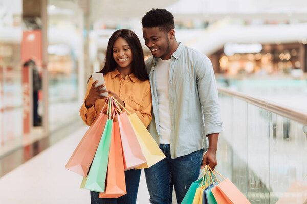 Портрет счастливой черной пары с помощью телефона с сумками для покупок