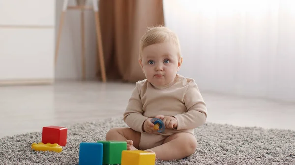 幸せな子供時代。可愛い小さな赤ちゃんはベッドルームで休んで、カラフルなおもちゃでカーペットの上に座ってペースメーカーを運ぶ, — ストック写真