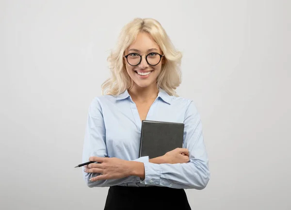 Retrato de empresaria feliz en ropa formal sosteniendo bloc de notas y bolígrafo, posando sobre fondo de estudio gris claro — Foto de Stock