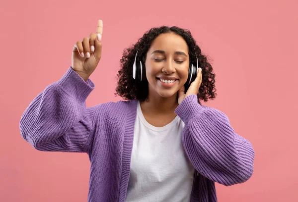 Hermosa joven negra escuchando música en auriculares inalámbricos, cerrando los ojos y apuntando hacia arriba — Foto de Stock