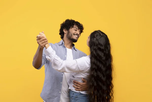 Любящие индийские пары держатся за руки и танцуют, обнимаются и улыбаются друг другу, имея свидание, желтый фон — стоковое фото