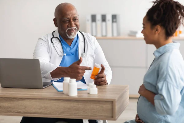 Starší zkušený černošky lékař ukazující pilulky těhotné dámě — Stock fotografie