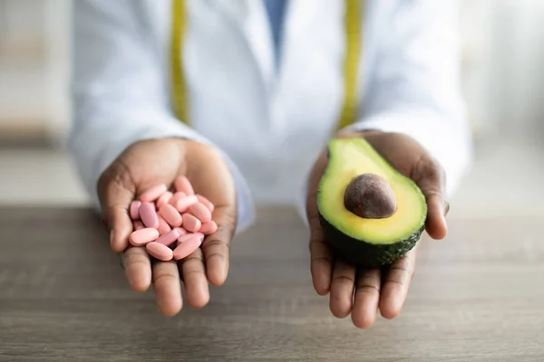 Здравоохранение и диета. Женщина-диетолог с кучей таблеток и половиной авокадо, работает в клинике, крупным планом — стоковое фото