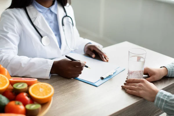 Detoks konsepti. Genç bayan hasta su içerken Afro-Amerikan diyetisyen diyetçi not alıyor, diyet planı yazıyor. — Stok fotoğraf