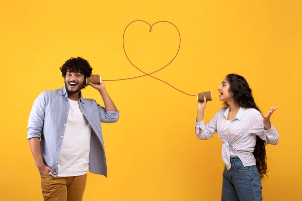 Lagu cinta. Wanita India yang penuh kasih mengirimkan pesan romantis kepada pacarnya melalui telepon kaleng, latar belakang kuning — Stok Foto